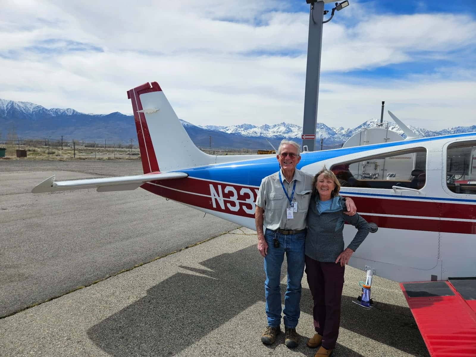 Volunteer pilot and passenger beside a mission aircraft in front of snow-capped mountains